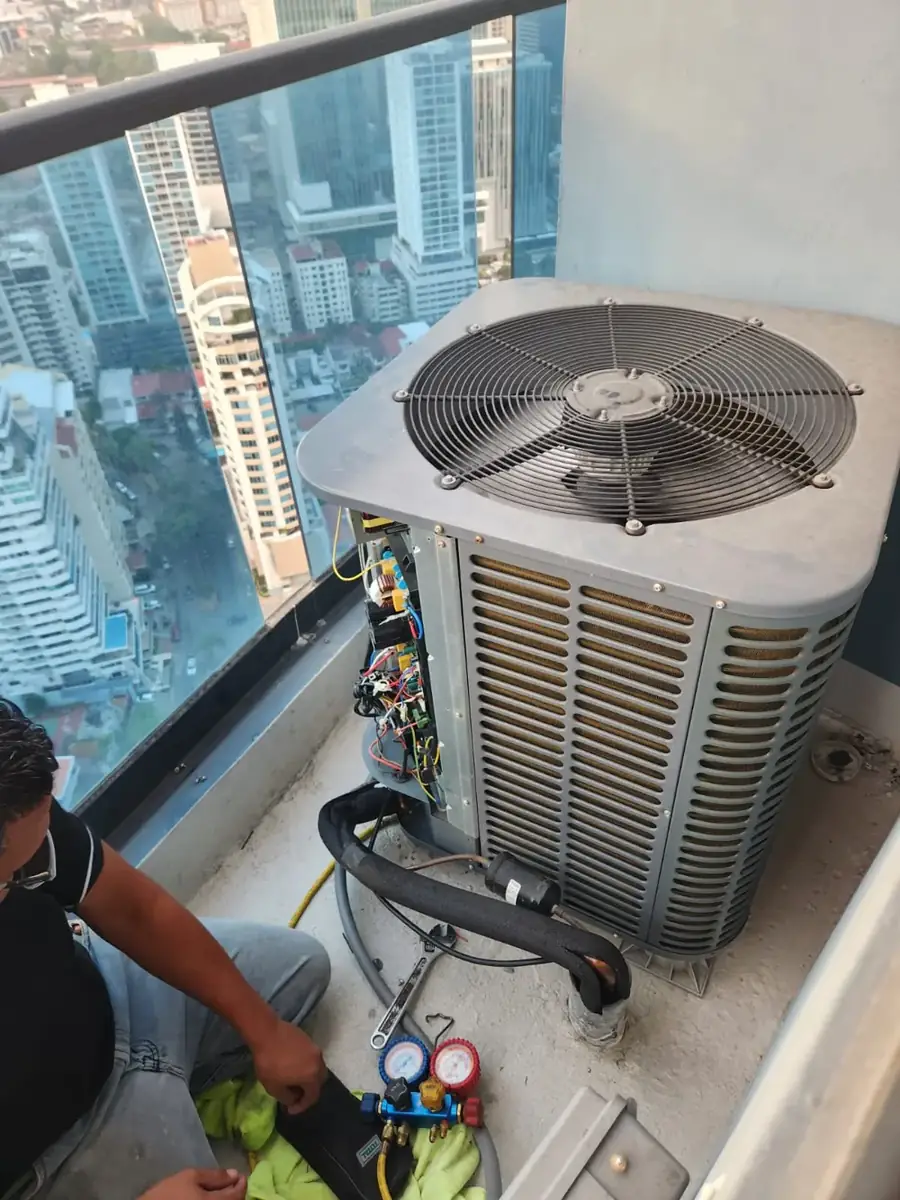 Técnico dando servicio a una unidad condensadora de aire acondicionado en un balcón